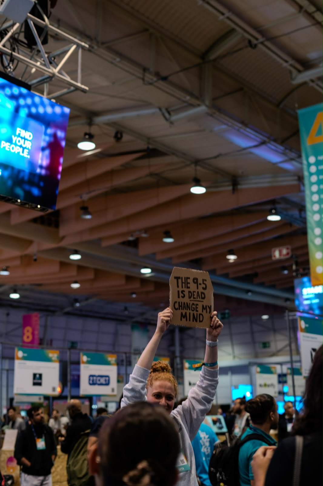 A person in the Web Summit crowd holding up a cardboard sign that reads: The 9-5 is dead, change my mind